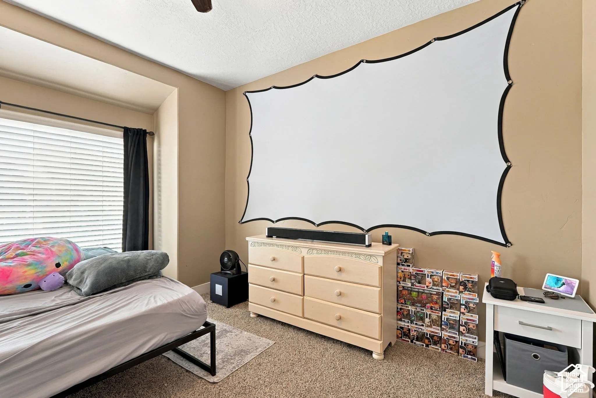 Large projection screen, recessed window with blinds, ceiling fan, carpeted flooring, and built-in dresser with decorative trim