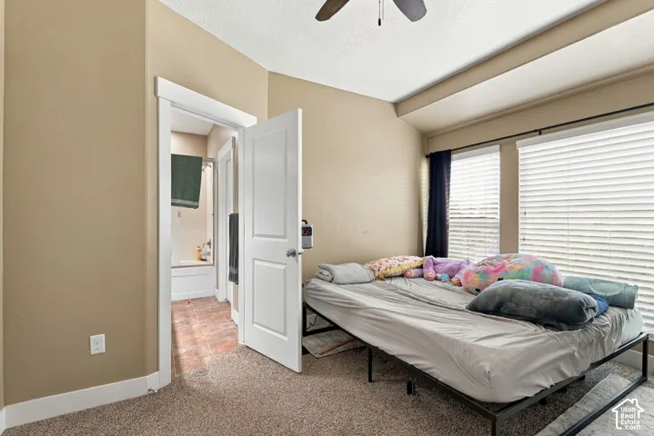 Carpet flooring with a ceiling fan, dual windows, and an en-suite bathroom featuring a shower-tub combination