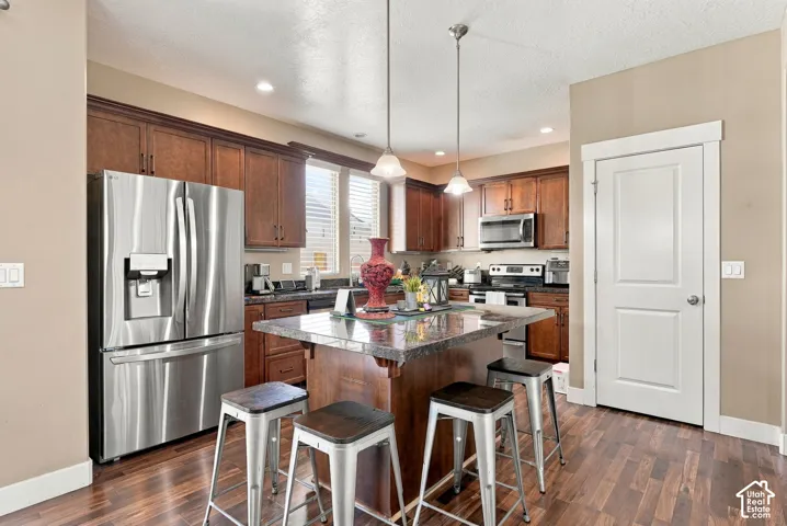 Kitchen with wood-finish flooring, dark wood cabinetry, a center island with countertop seating, stainless steel appliances, and recessed lighting