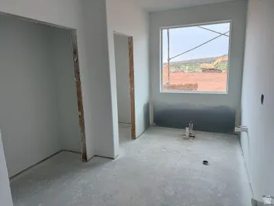 Unfinished room with light gray wall paint, a large rectangular window, and exposed plumbing rough-ins