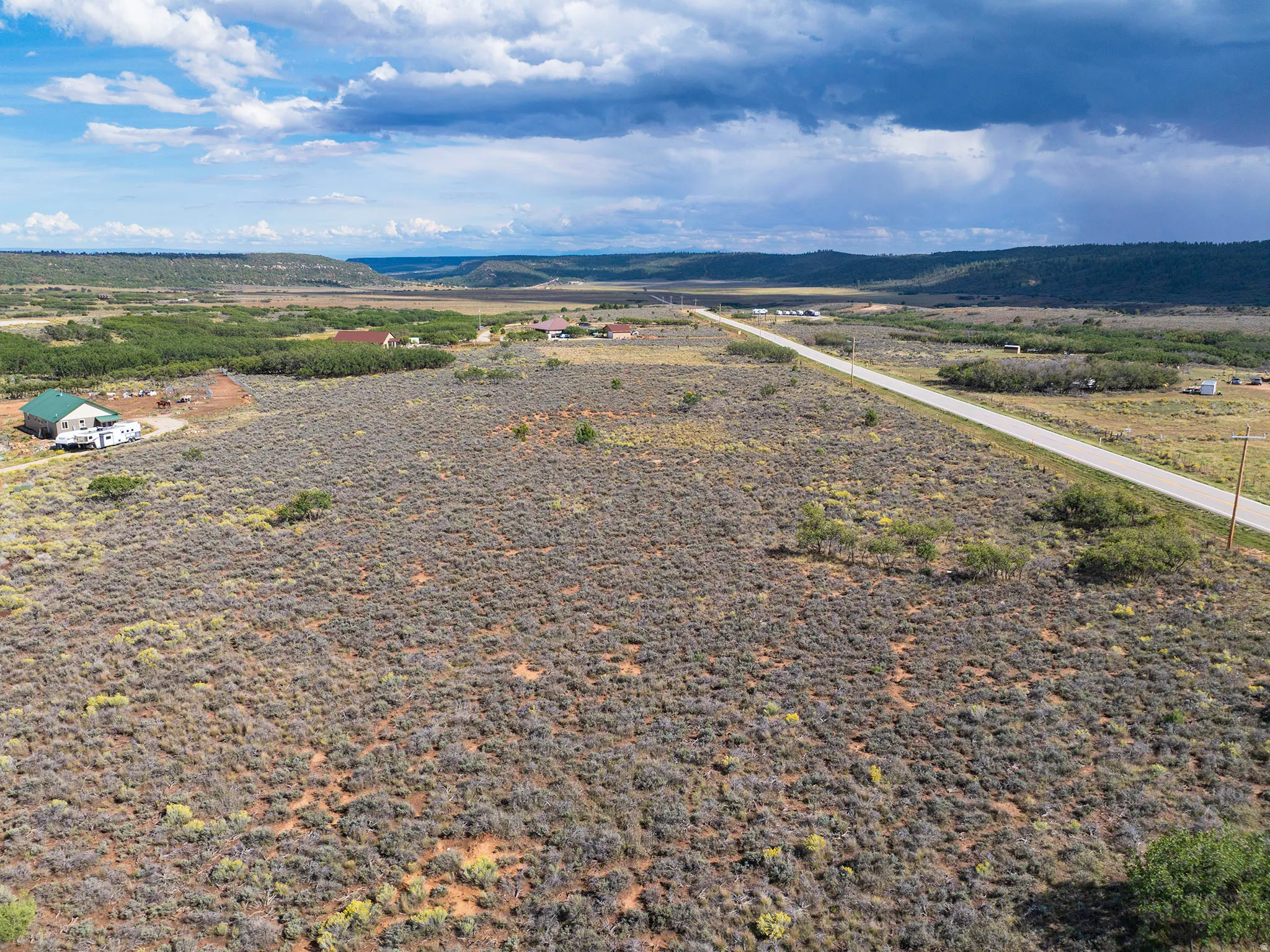 Expansive rural landscape featuring a paved road, scattered structures, and distant natural terrain