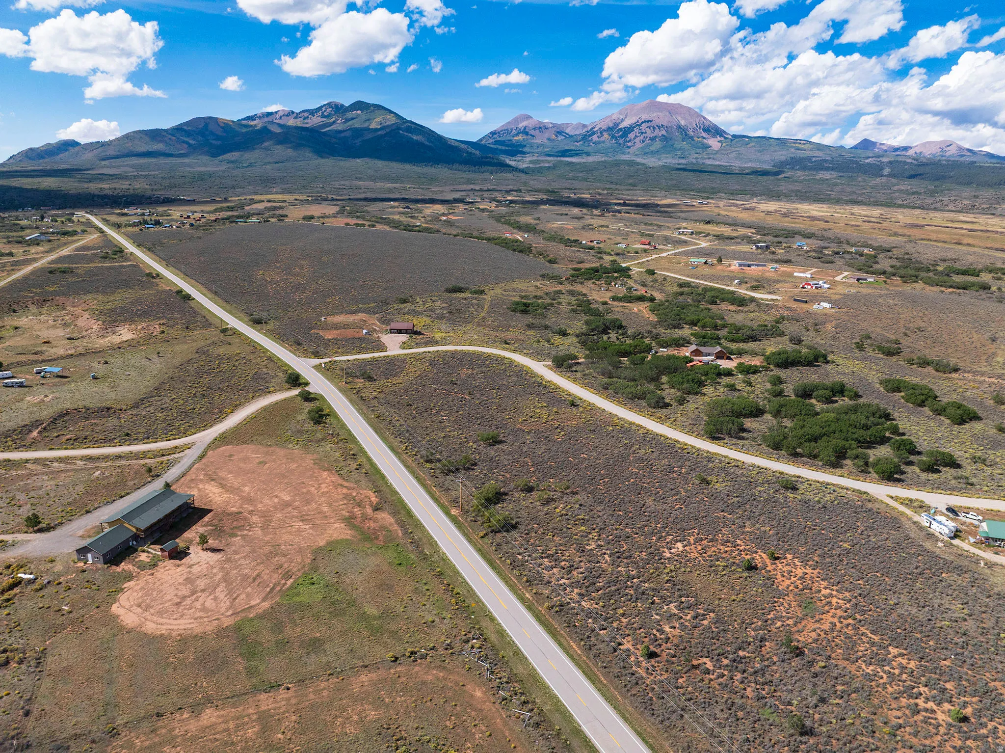 Expansive rural landscape featuring a paved road, scattered residences, and distant mountains