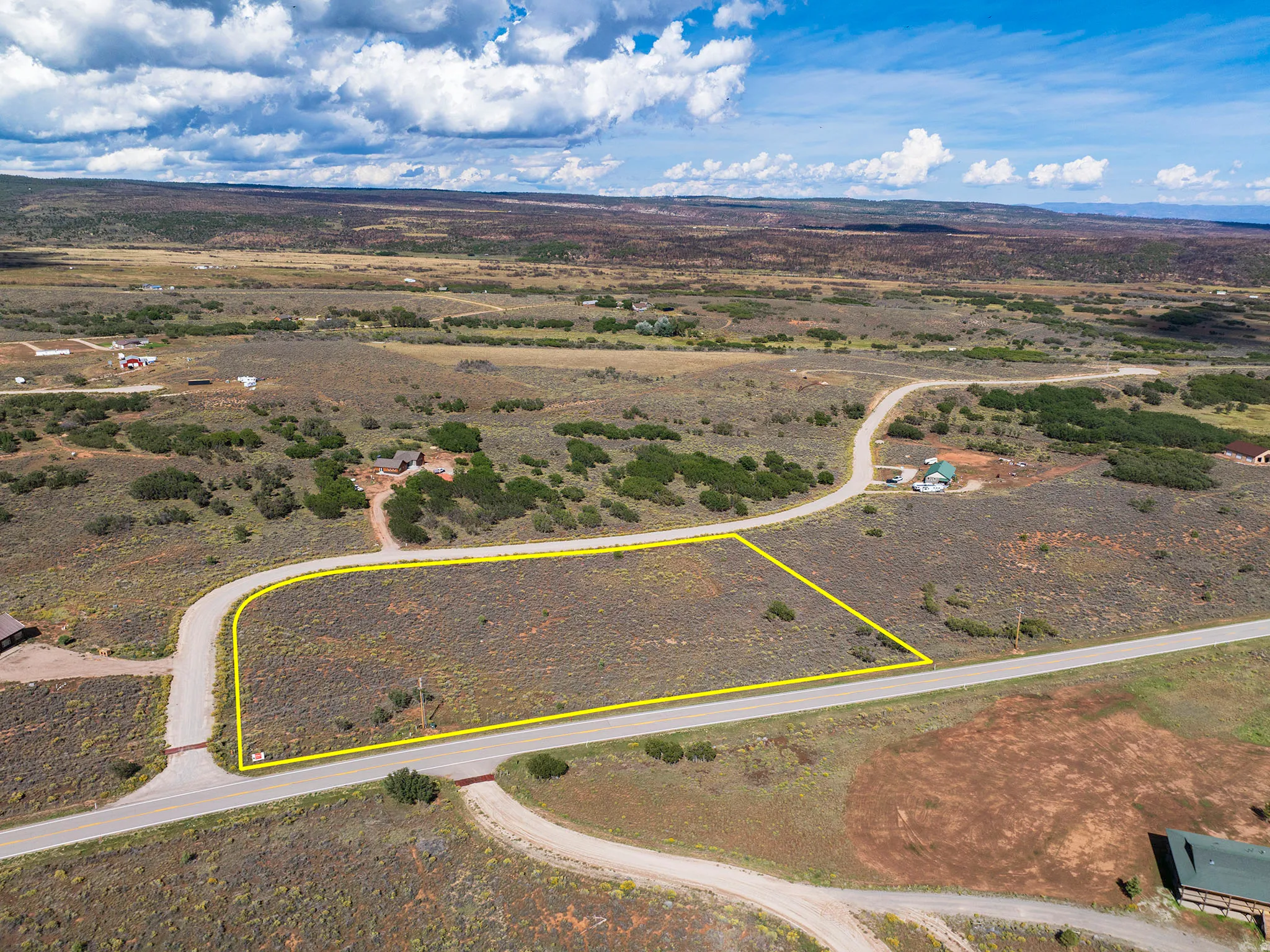 Expansive undeveloped lot featuring a paved road frontage, natural vegetation, and a wide-open landscape