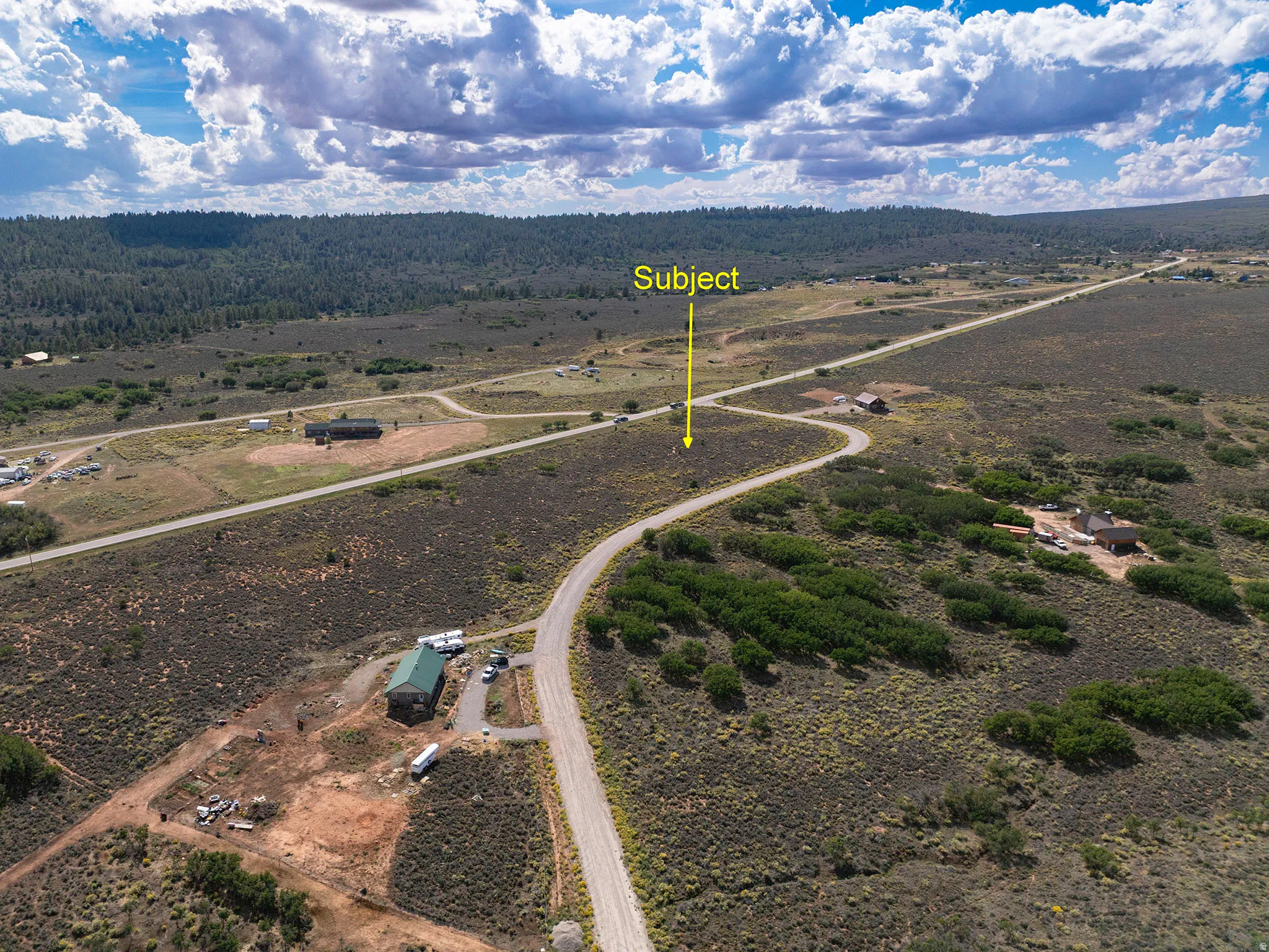 Expansive undeveloped land with a curving dirt road, surrounded by low-growing vegetation and distant trees