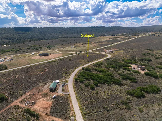 Expansive undeveloped land with a curving dirt road, surrounded by low-growing vegetation and distant trees