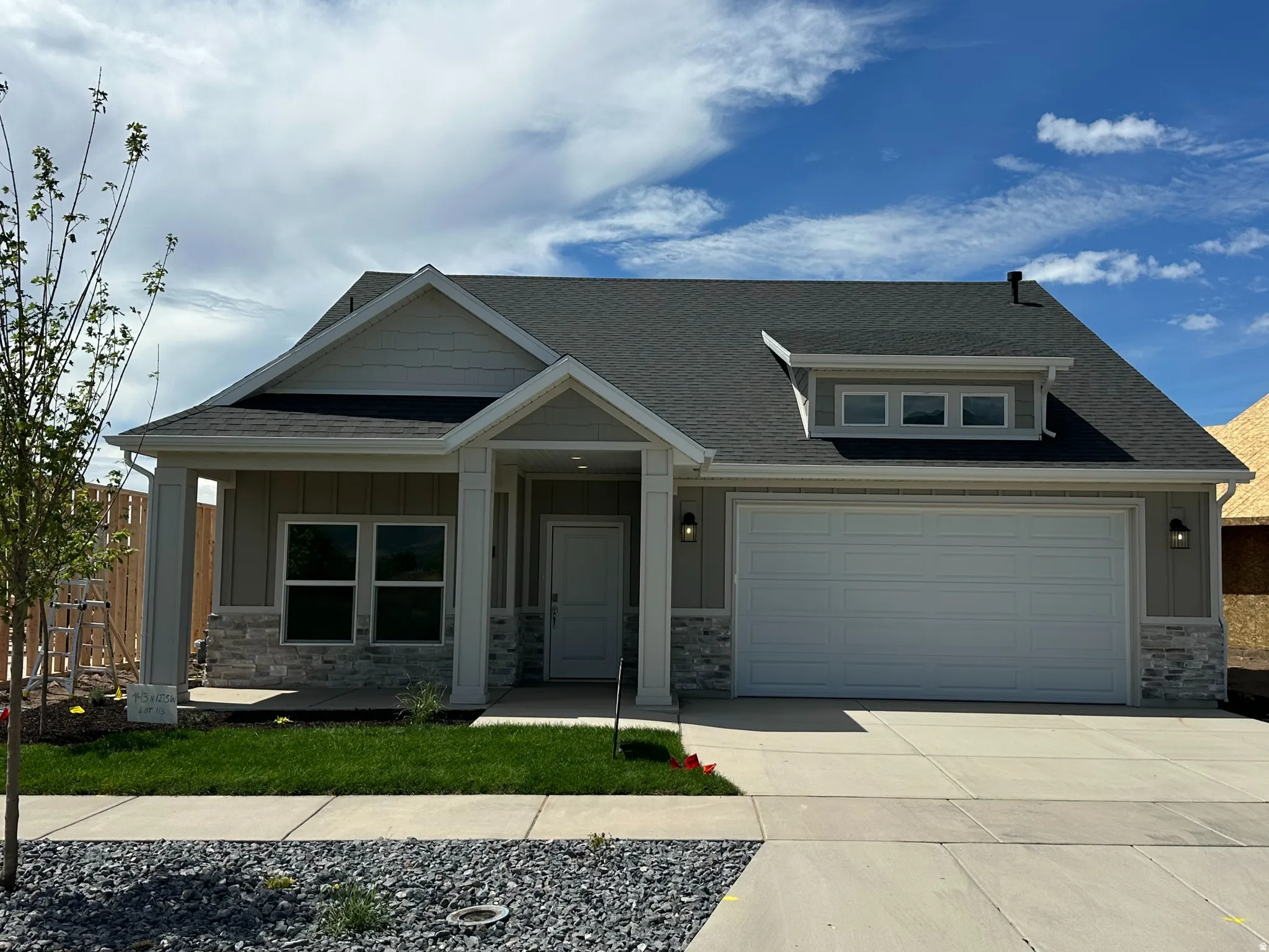 Modern exterior featuring stone and siding accents, a dark shingle roof, an integrated garage, a front entry porch, and a manicured lawn