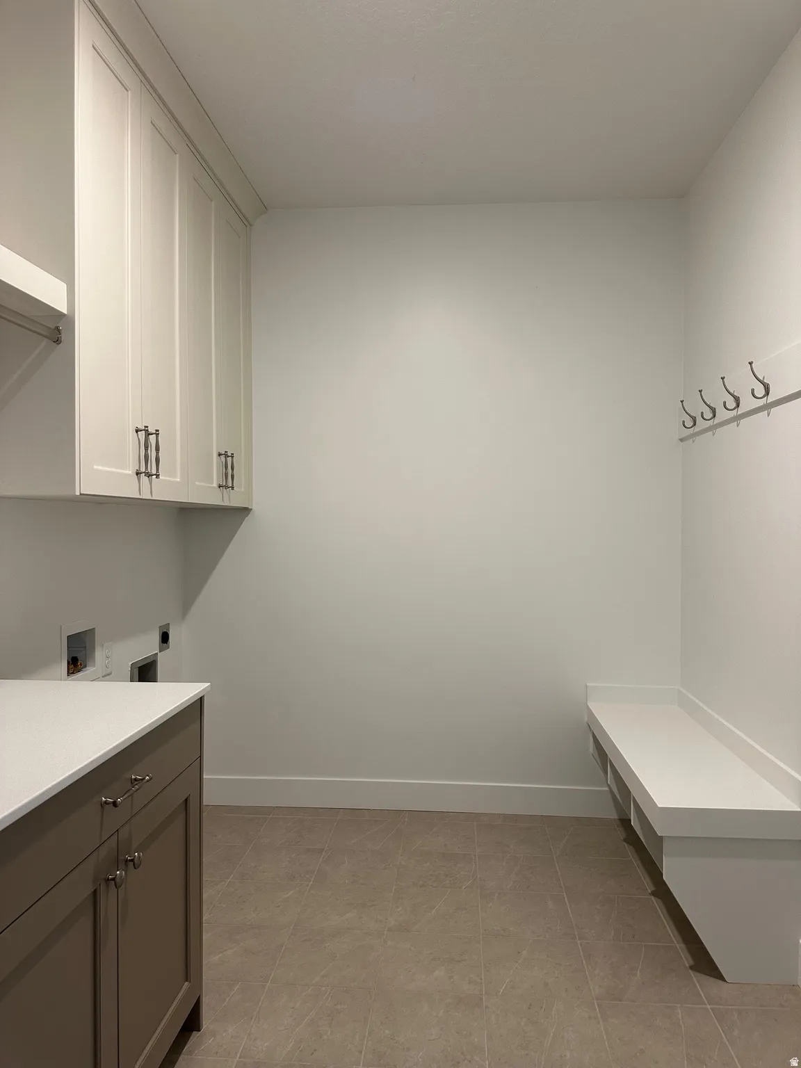 Neutral-toned floor tile, built-in storage cabinets with white shaker doors, integrated white countertop, base cabinets with neutral-toned doors, and a built-in bench