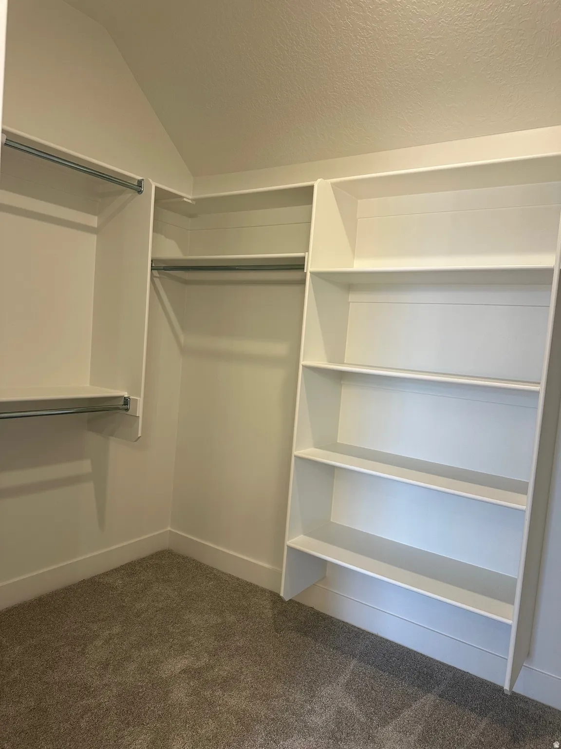 Custom closet system with white shelving, multiple hanging rods, and textured carpeting