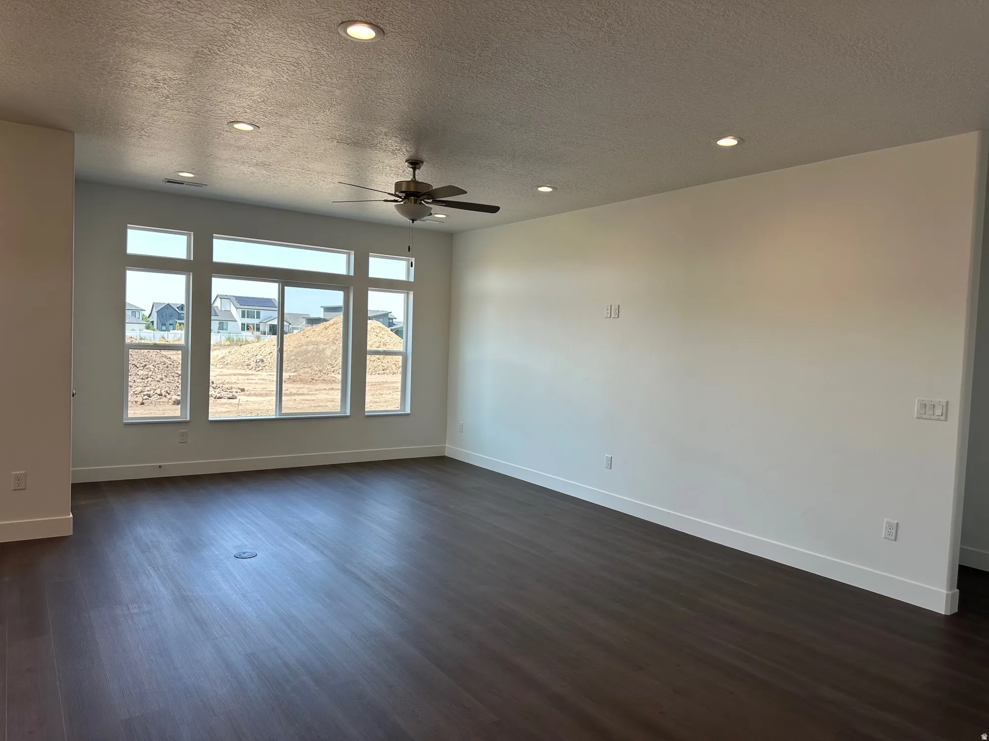 Expansive room featuring multiple picture windows, dark wood-finish flooring, a ceiling fan, and recessed lighting