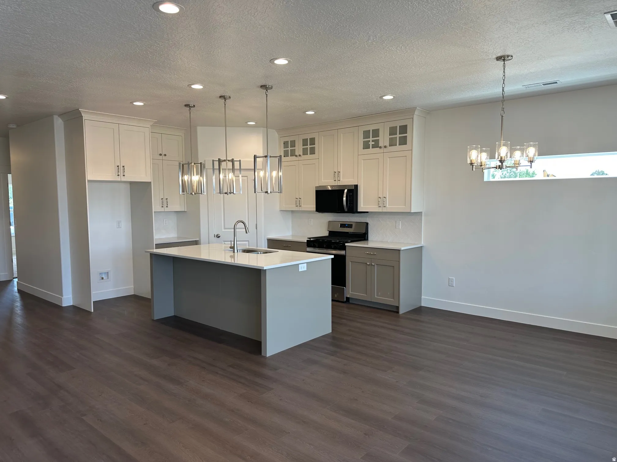 Open-concept kitchen featuring an island with a sink, stainless steel appliances, white shaker cabinetry, and wood-finish flooring