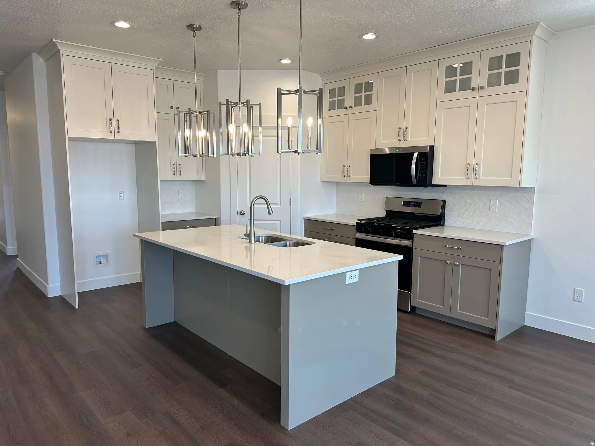 Gourmet kitchen with wood-finish flooring, a central island featuring a stainless steel sink, and white upper cabinetry with glass-front accents