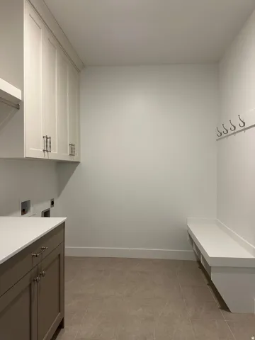 Neutral-toned floor tile, built-in storage cabinets with white shaker doors, integrated white countertop, base cabinets with neutral-toned doors, and a built-in bench