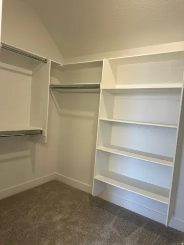 Custom closet system with white shelving, multiple hanging rods, and textured carpeting