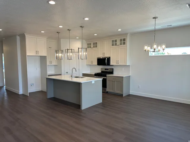 Open-concept kitchen featuring an island with a sink, stainless steel appliances, white shaker cabinetry, and wood-finish flooring