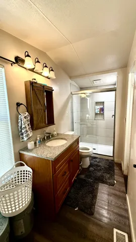 Dual-sink vanity with a granite-style countertop, wood-finish cabinetry, and contemporary light fixture. Master bathroom