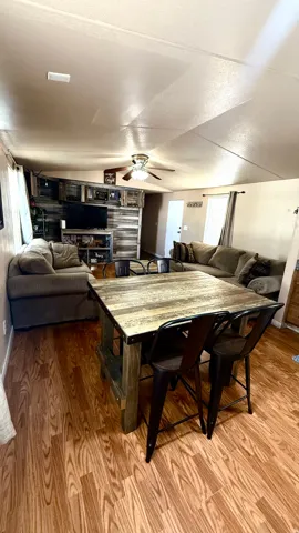 Wood-finish flooring throughout, ceiling fan with integrated lighting, and a prominent media wall with integrated shelving