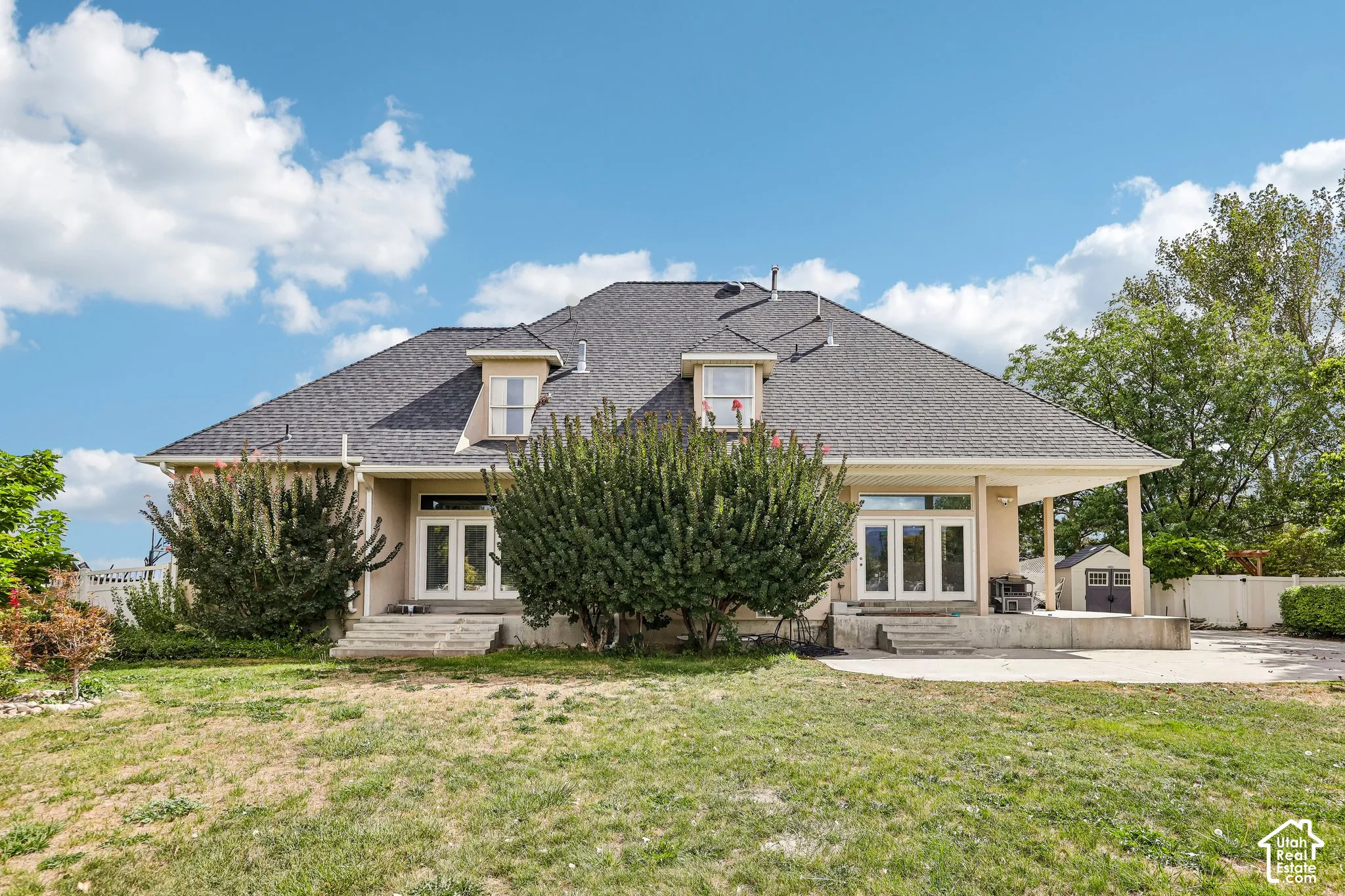 Spacious rear exterior featuring a covered patio, multiple sets of double doors, upper-level dormer windows, and a detached storage shed