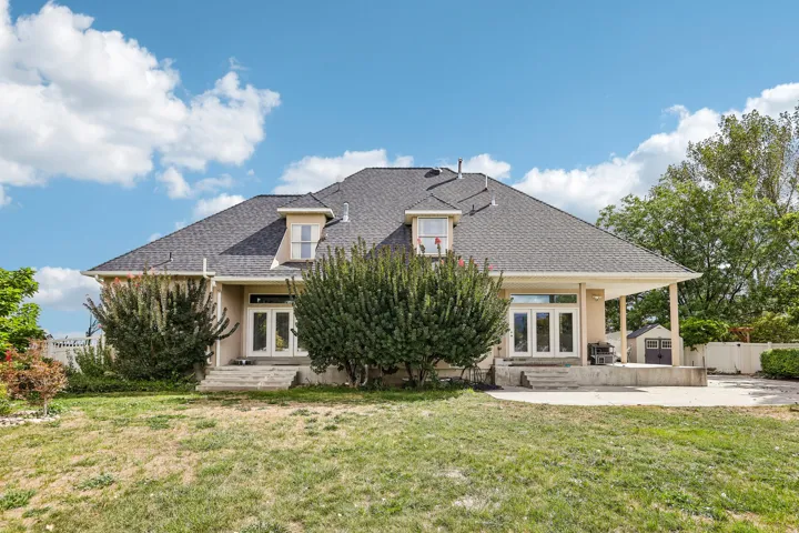 Spacious rear exterior featuring a covered patio, multiple sets of double doors, upper-level dormer windows, and a detached storage shed
