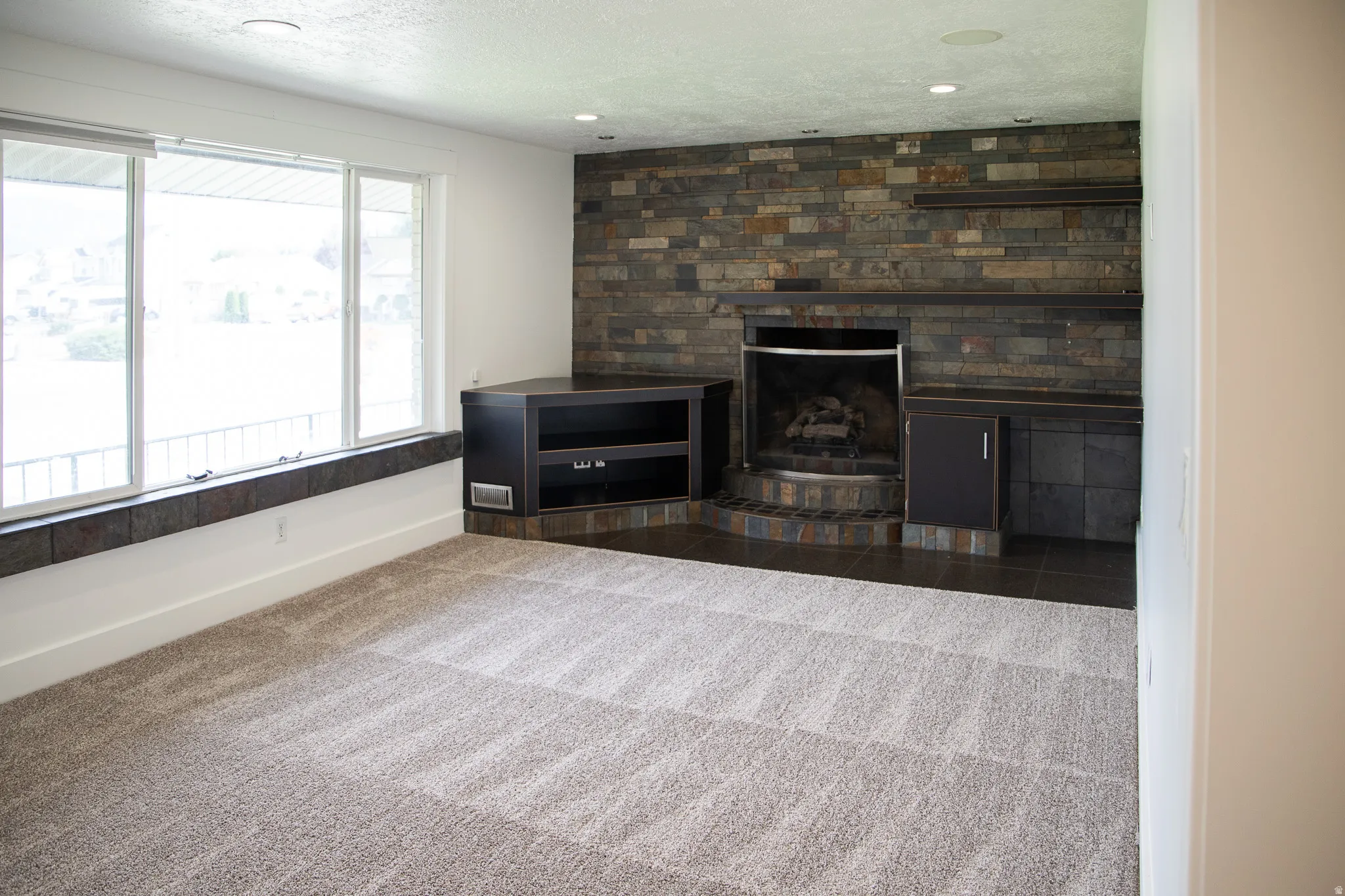 Expansive window, stone-clad fireplace, built-in cabinetry, recessed lighting, and carpet flooring