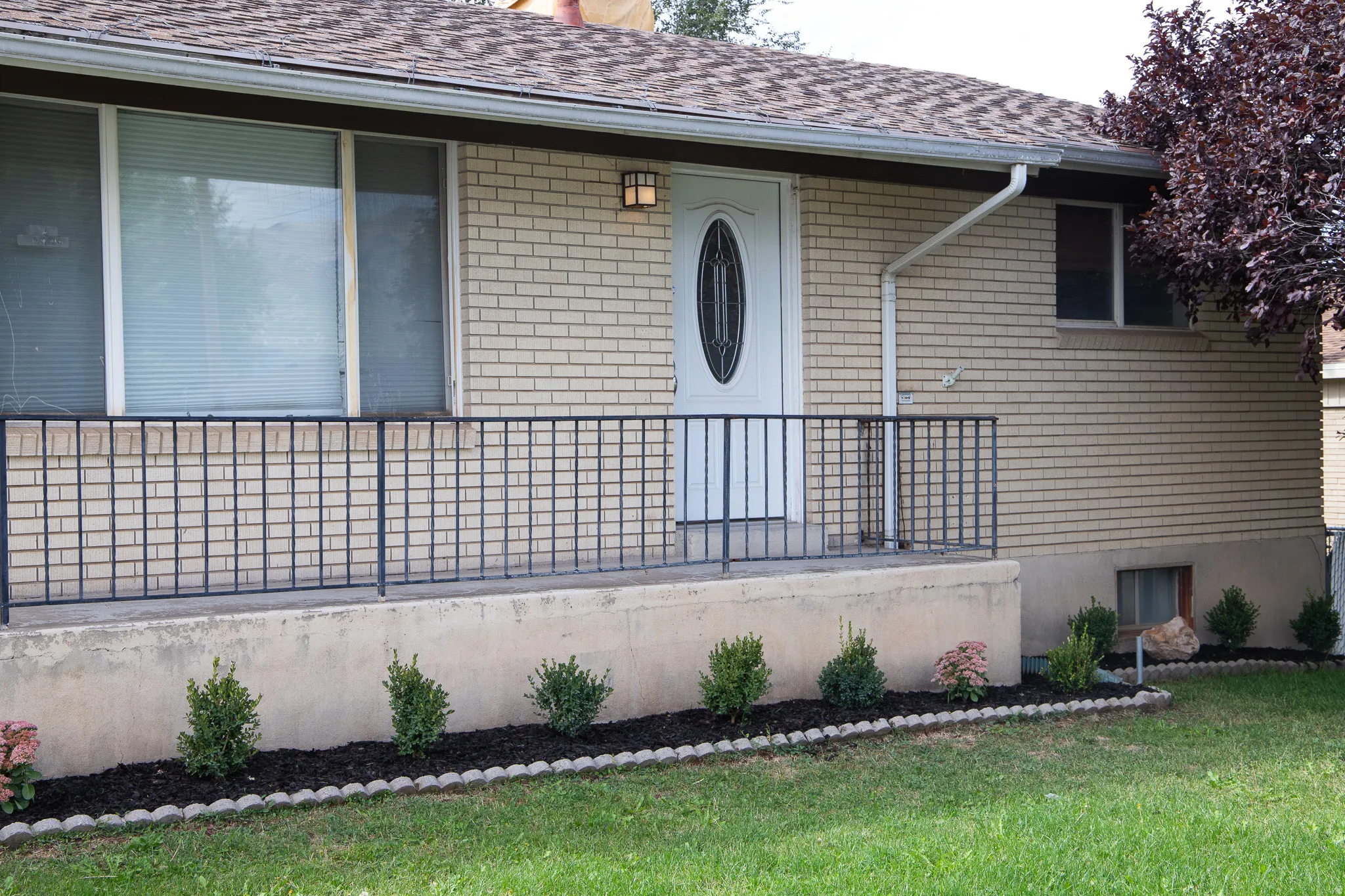 Brick exterior with a covered porch, oval-paneled entry door, and dark metal railing