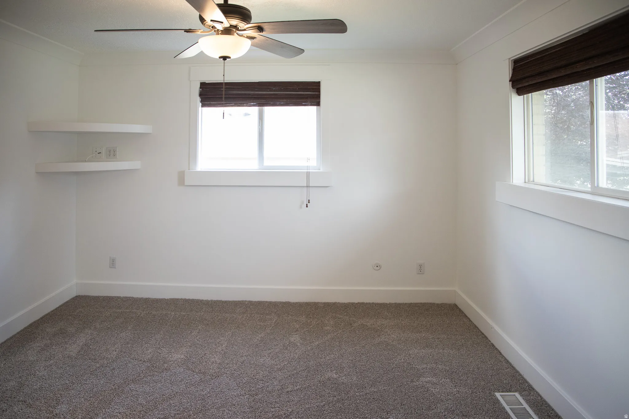 Recessed lighting with a ceiling fan, dual windows with custom window treatments, corner floating shelves, and plush carpeting