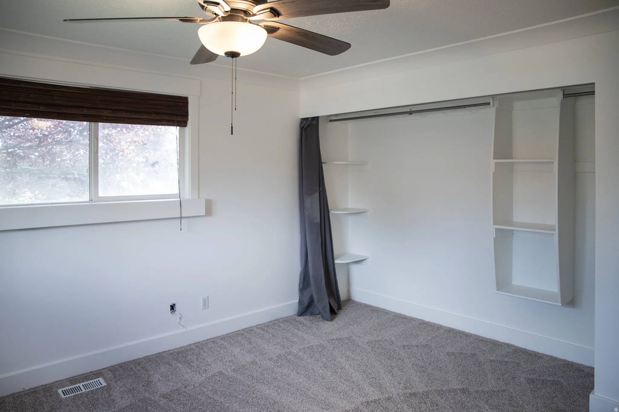 Recessed window featuring a woven wood shade, ceiling fan with integrated lighting, built-in shelving, and carpeted flooring