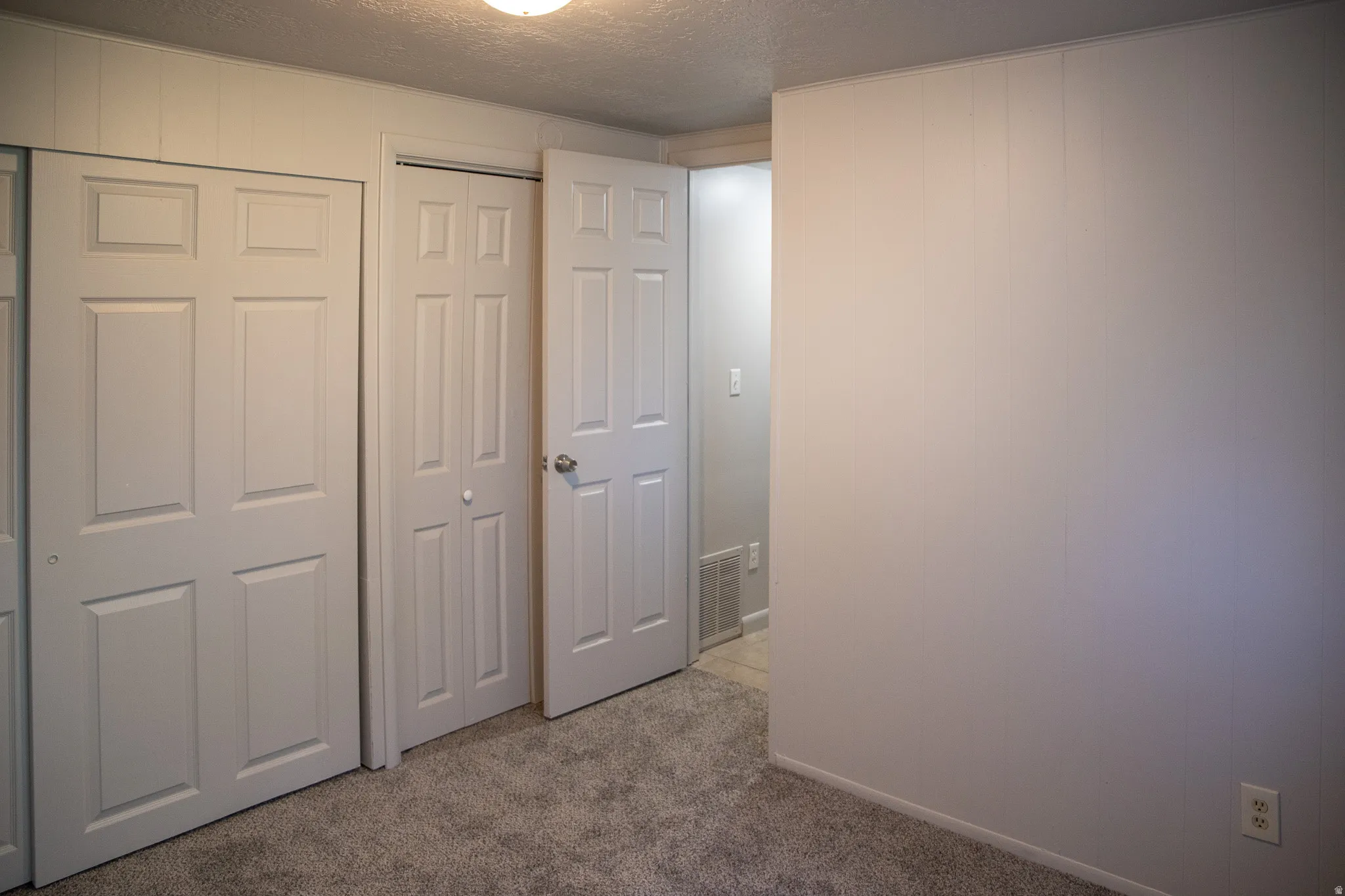 Wall-to-wall carpeting with multiple closet doors and a paneled accent wall
