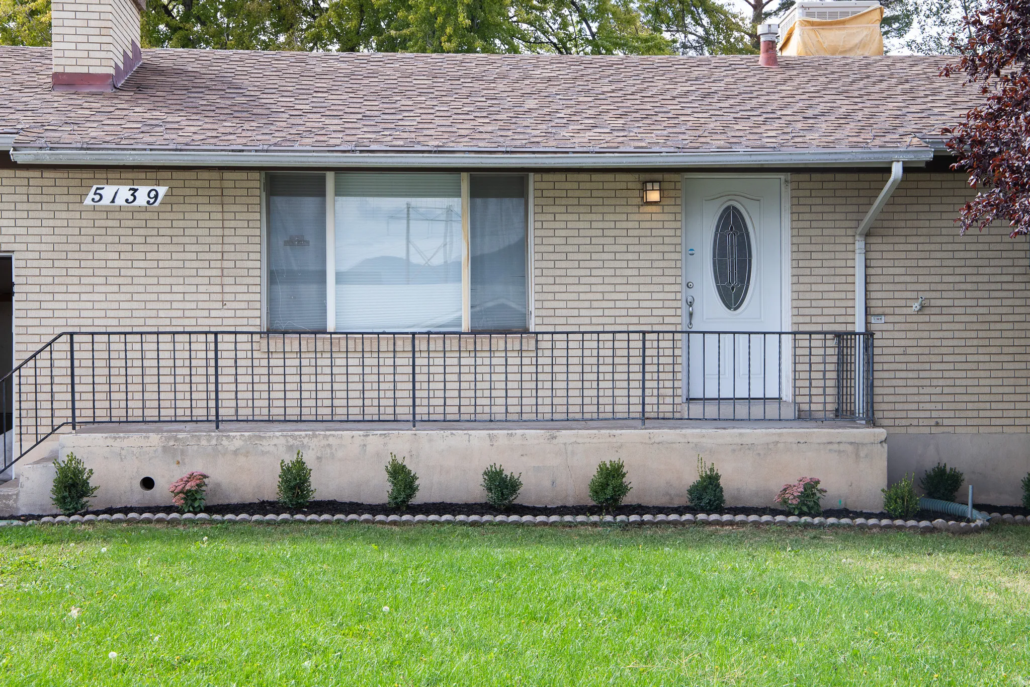 Brick facade with a shingle roof and front porch featuring a decorative railing