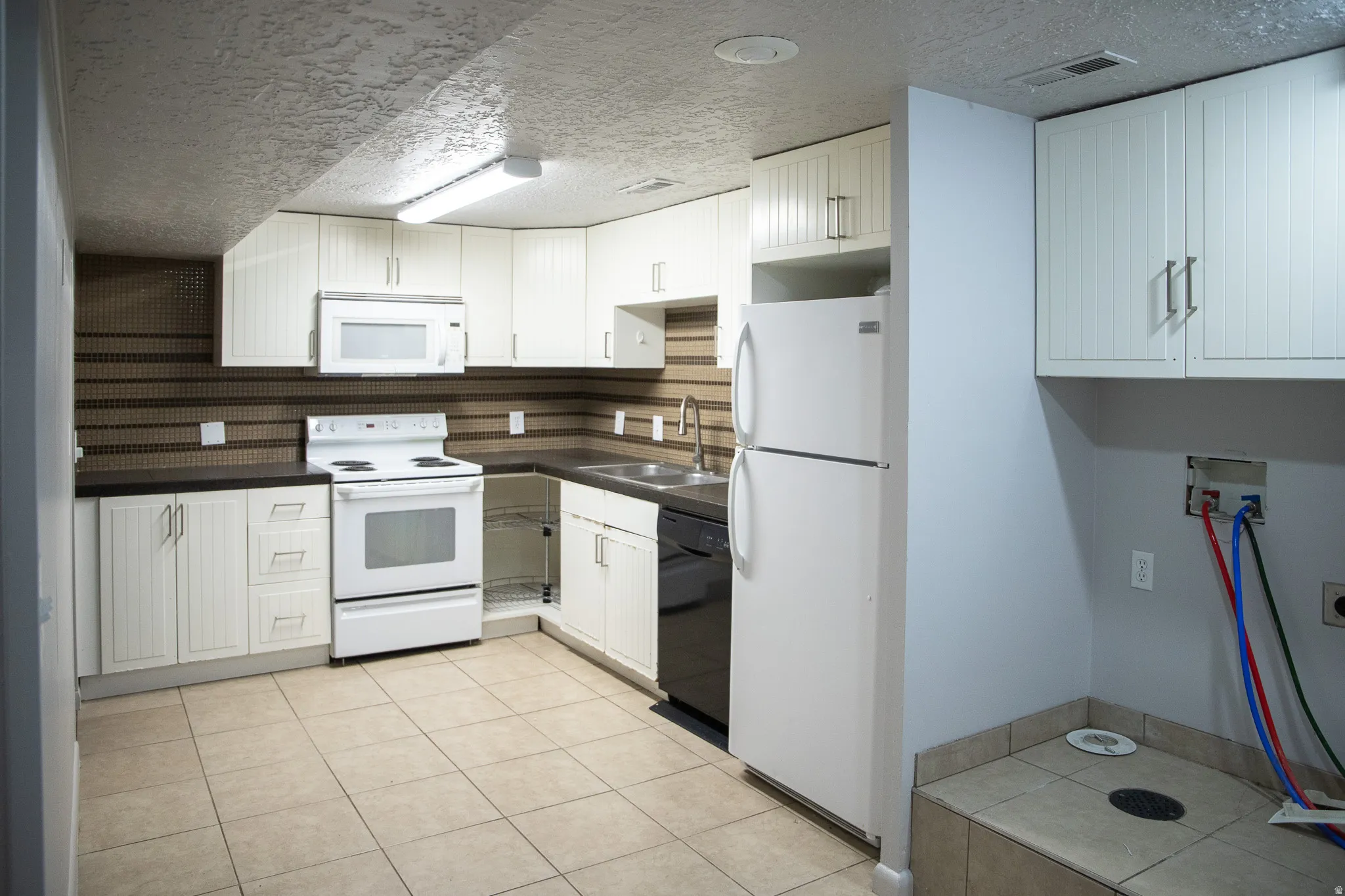 Kitchen featuring white cabinetry, dark countertops, a tile backsplash, and a white appliance package