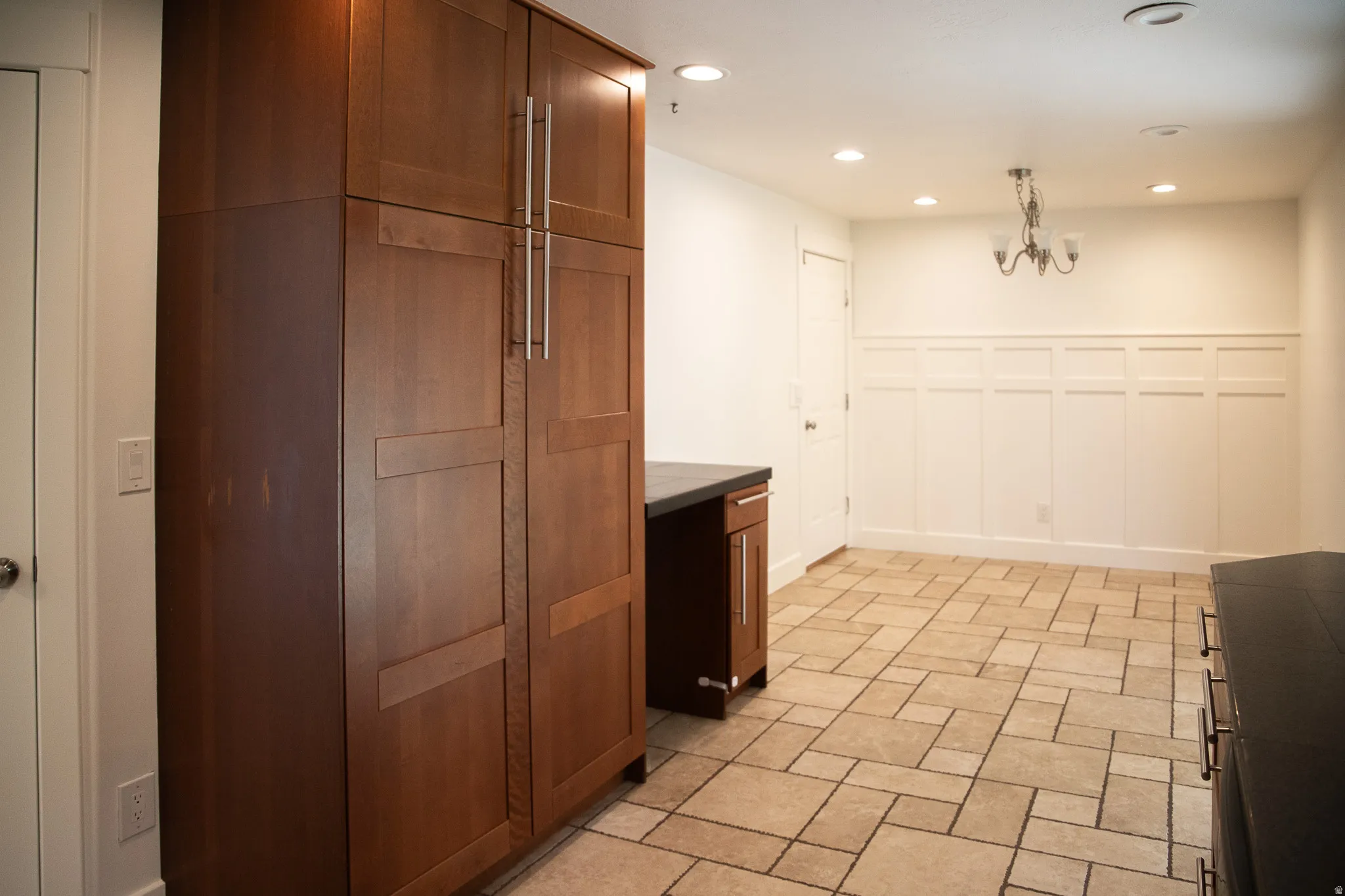 Built-in wood-finish cabinetry, tile flooring, recessed lighting, chandelier, and white wainscoting