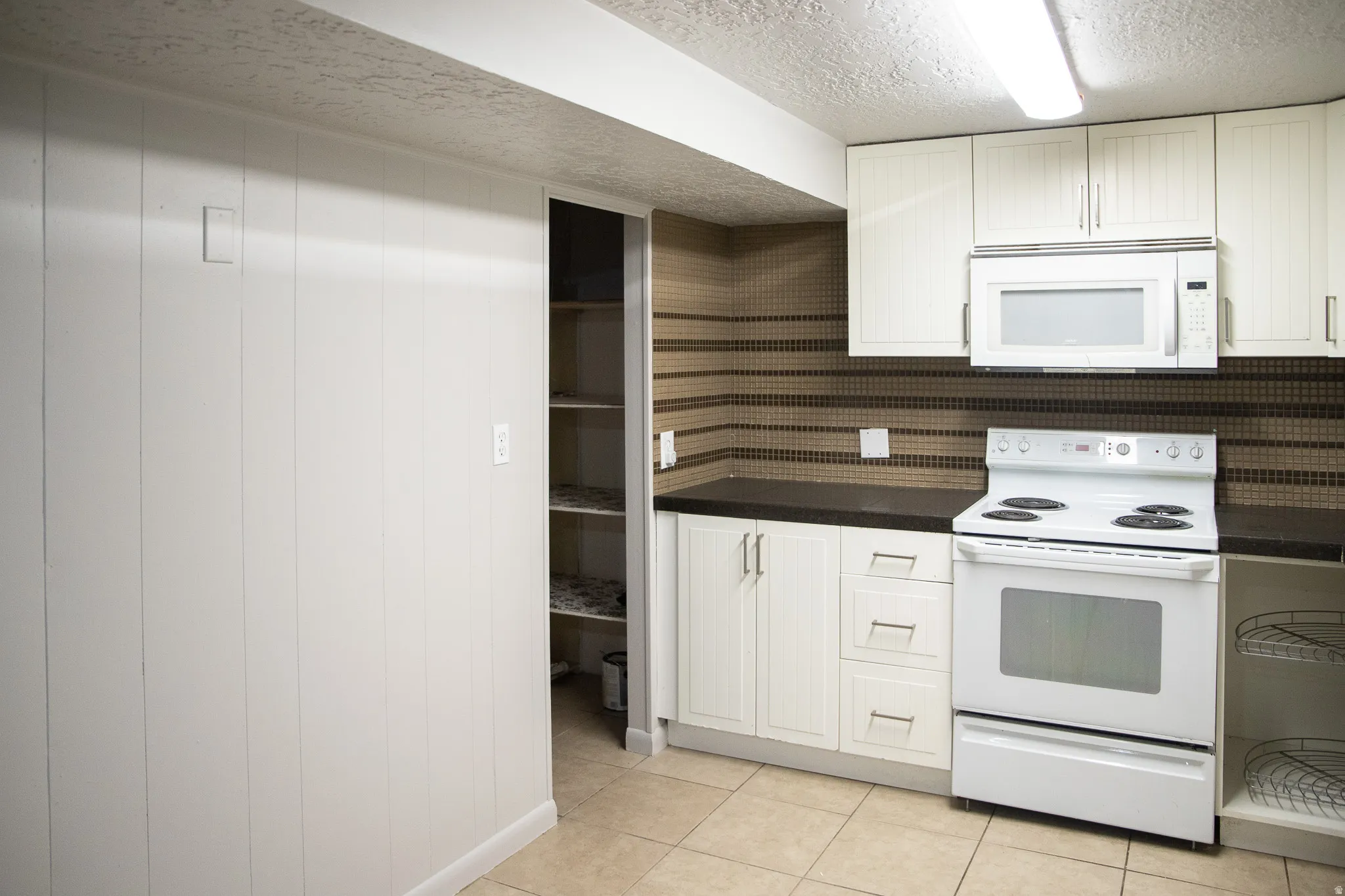 Kitchen featuring white cabinetry, dark countertops, a tiled backsplash, and tile flooring