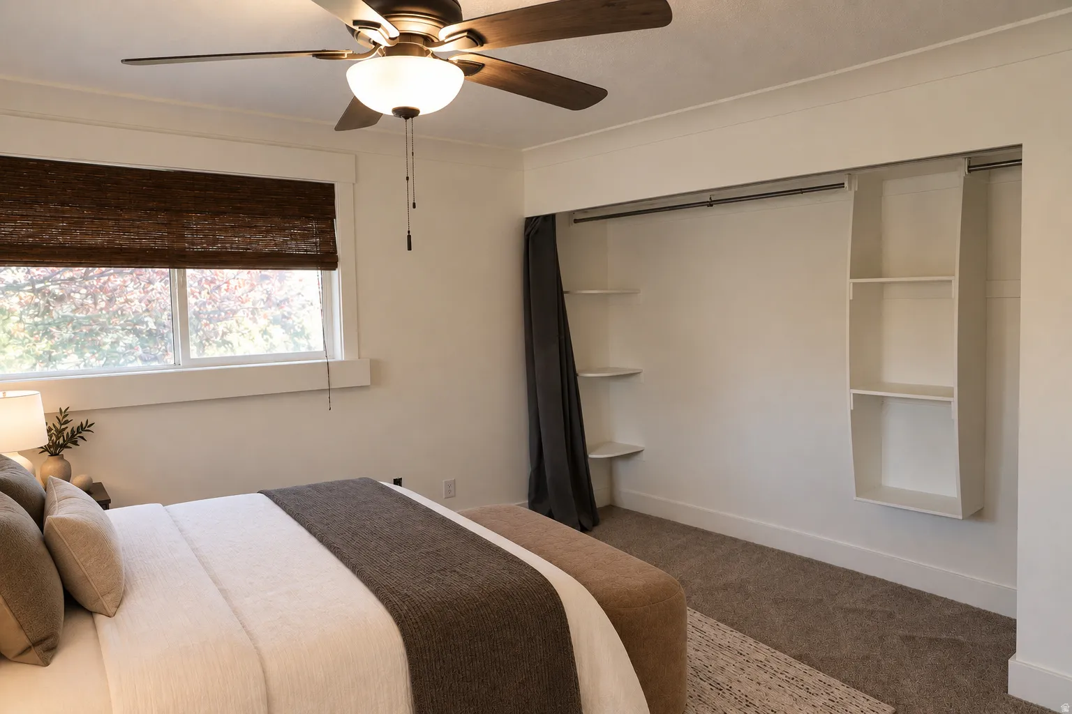 Ceiling fan with integrated lighting, window with a woven blind, built-in closet shelving, and a wall-mounted hanging rod
