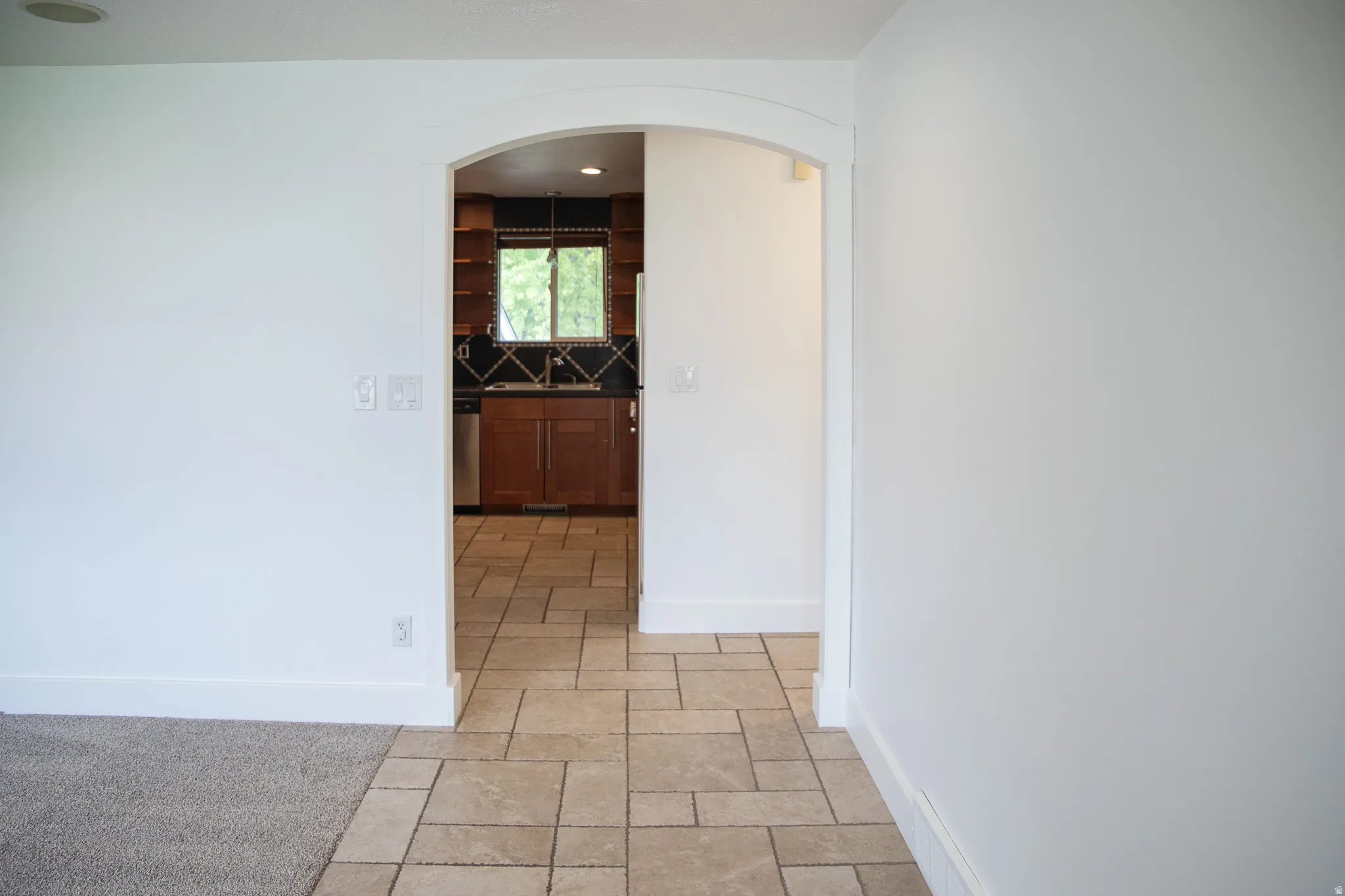 Archway entry leading to kitchen with wood cabinetry, stainless steel appliances, and a tiled backsplash