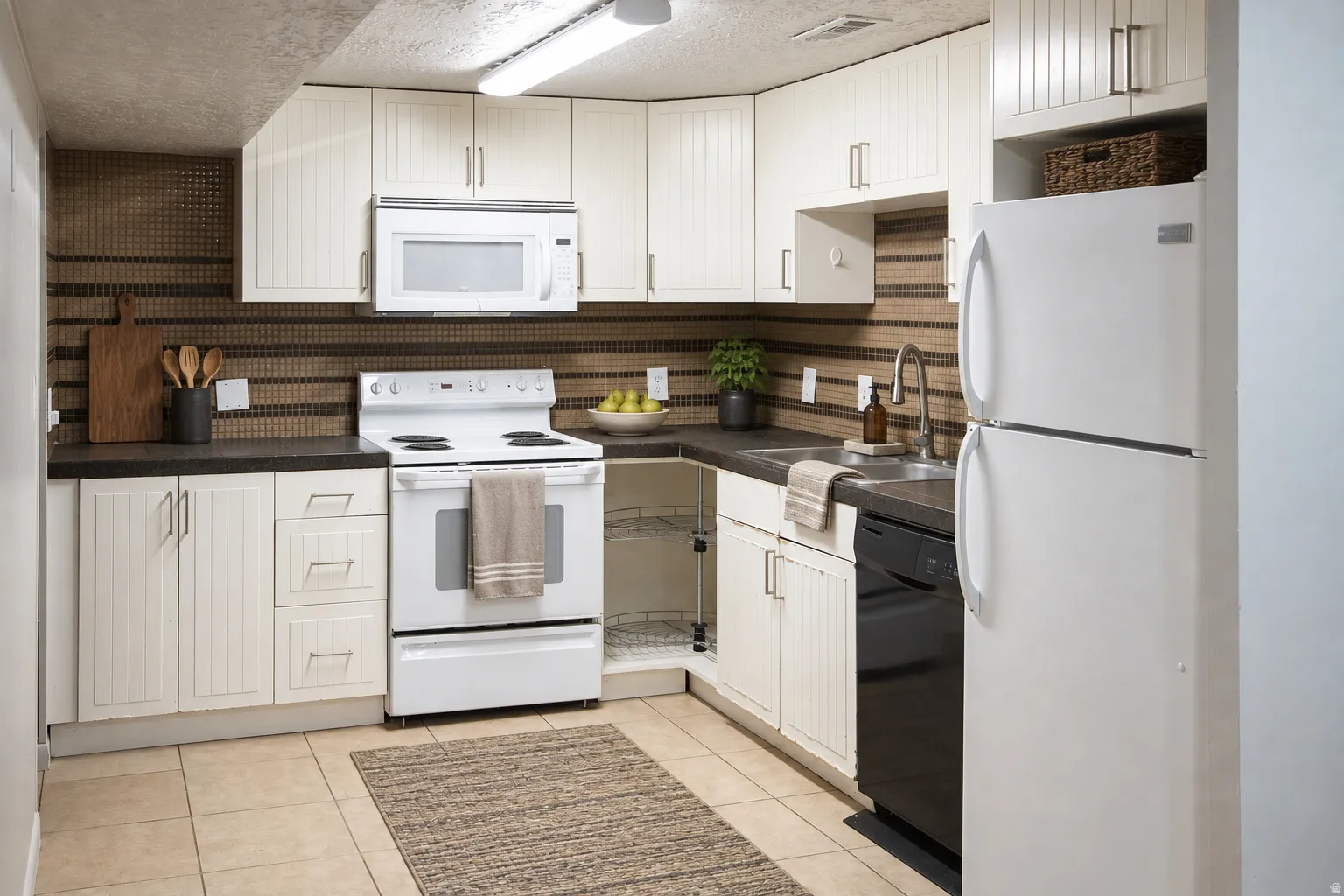 Full kitchen featuring white cabinetry, black countertops, a built-in microwave, and a white refrigerator
