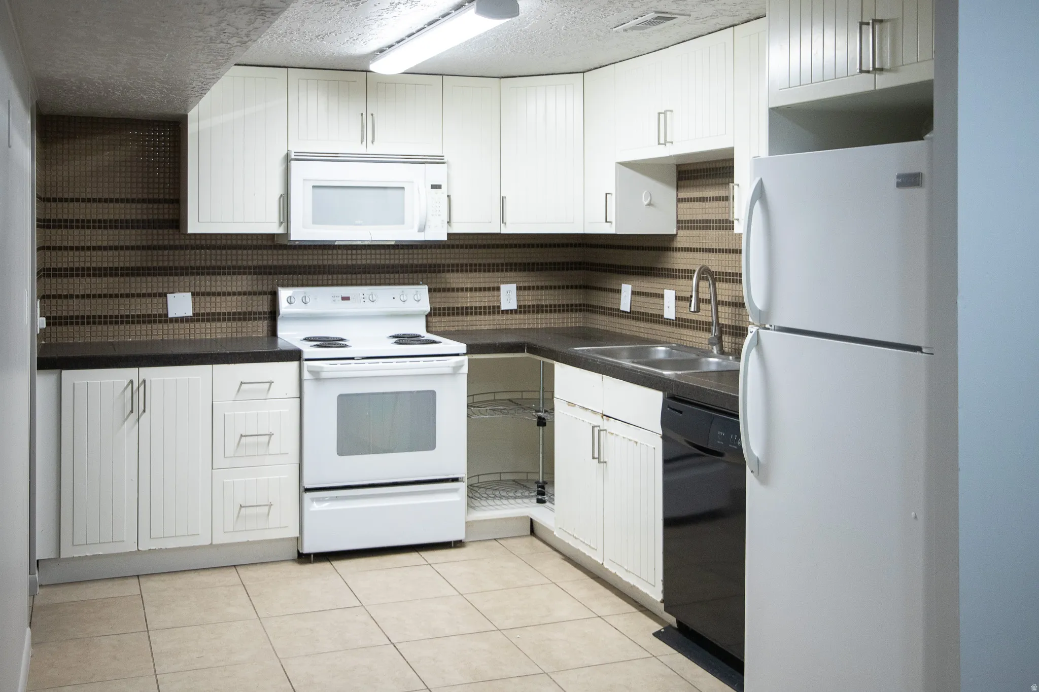 Kitchen with white cabinetry, dark countertops, tile backsplash, tile flooring, and integrated appliances