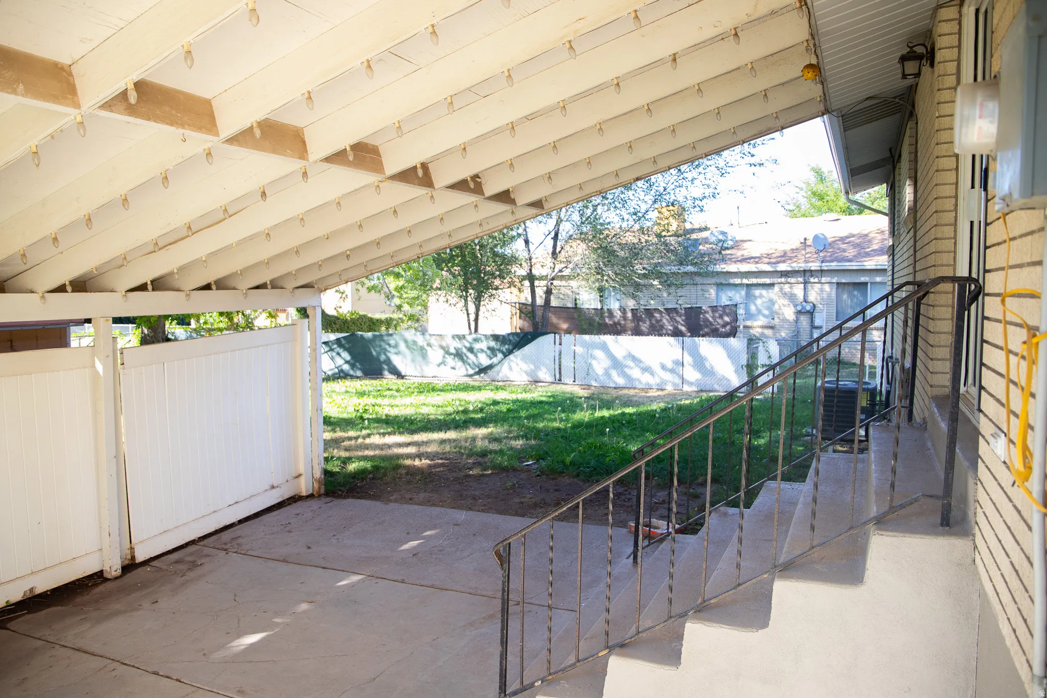 Covered patio with concrete flooring, white slatted privacy fence, and metal handrail leading to a brick exterior