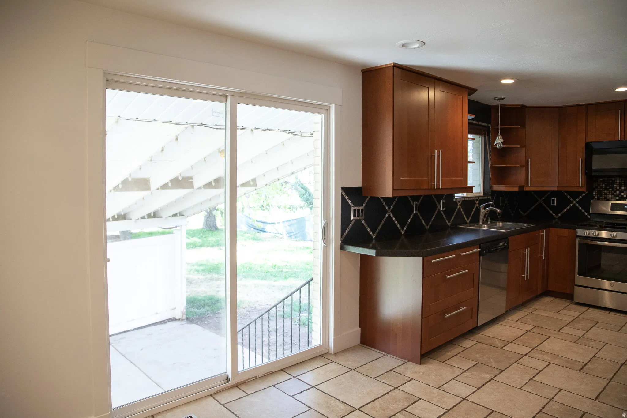 Kitchen featuring wood cabinetry, stainless steel appliances, black countertops, and a decorative tile backsplash