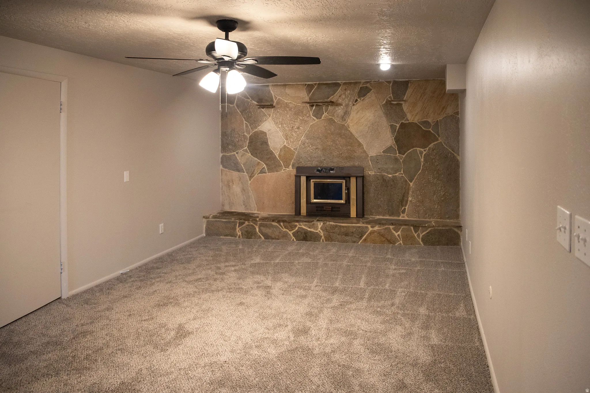 Natural stone accent wall with built-in fireplace, wall-to-wall carpeting, and a ceiling fan with integrated lighting