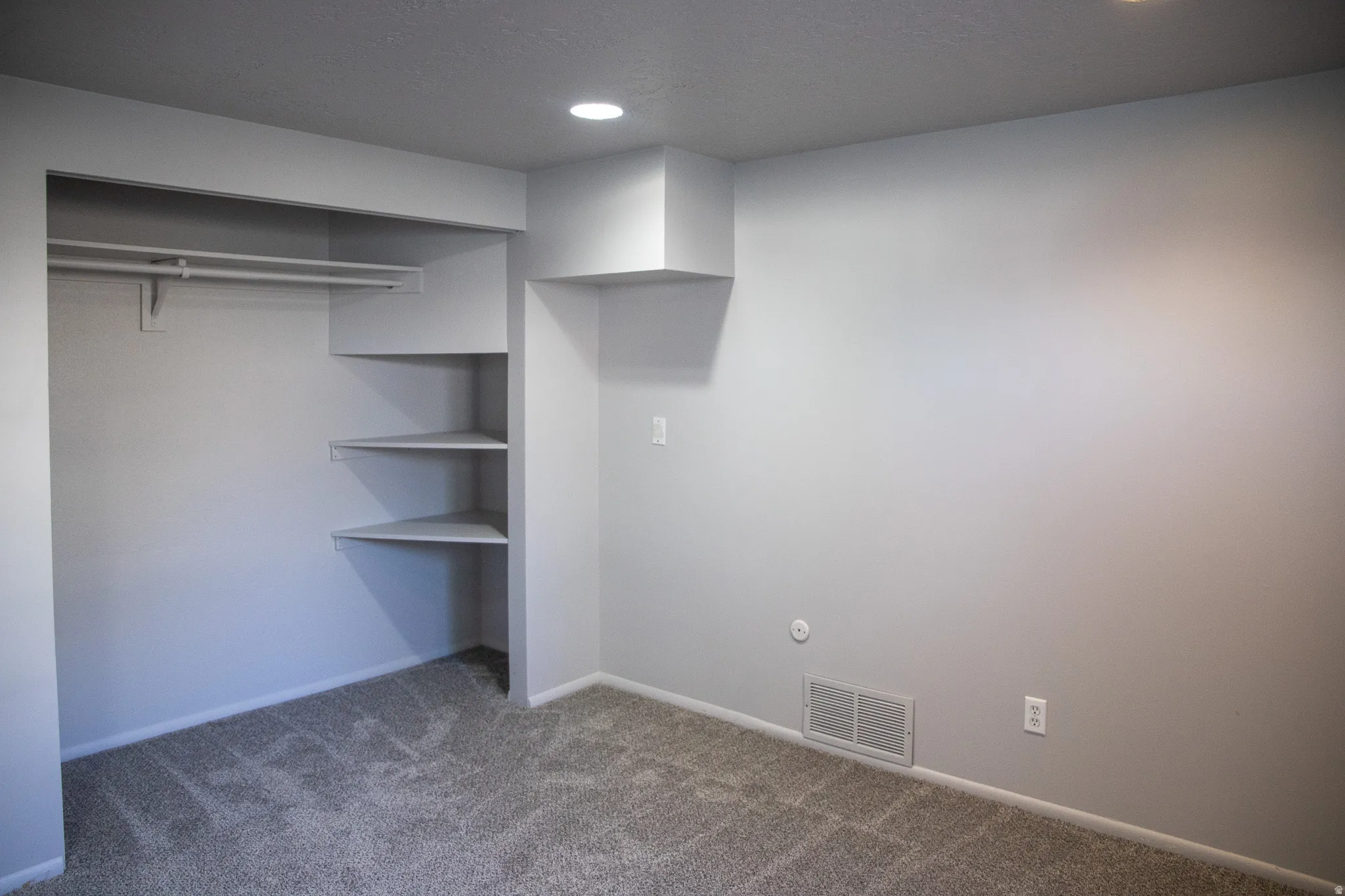 Built-in closet system with hanging rod and corner shelving, light gray wall finishes, recessed lighting, and textured carpet flooring