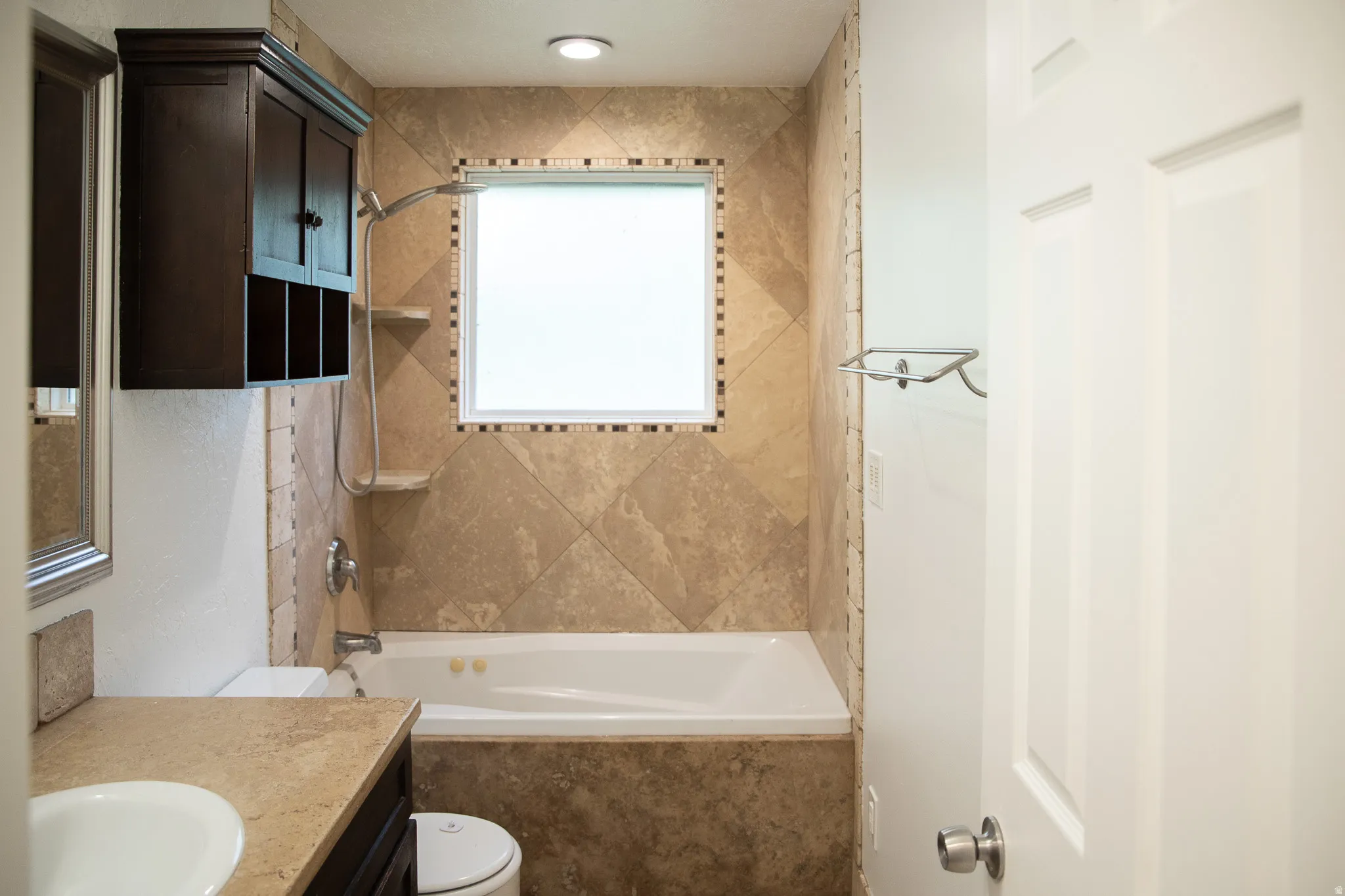 Tiled bath enclosure with a built-in tub, decorative tile accents, and an overhead shower fixture
