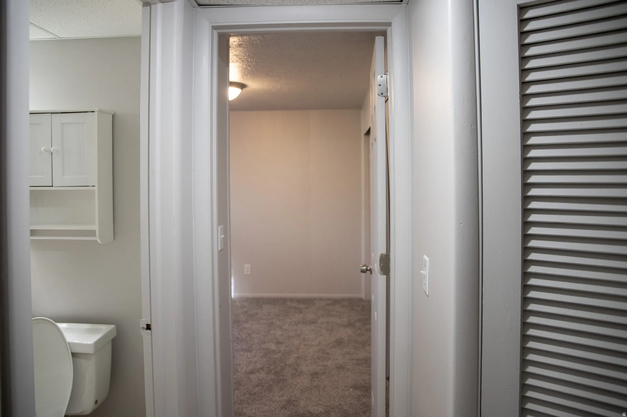 White wall-mounted cabinetry, a white toilet, and louvered bifold closet doors
