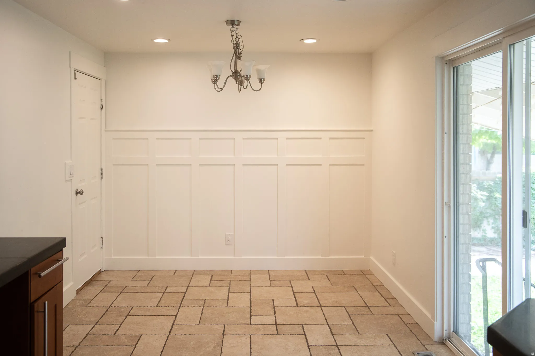 Paneled accent wall, recessed lighting, chandelier, sliding glass door, and tiled flooring