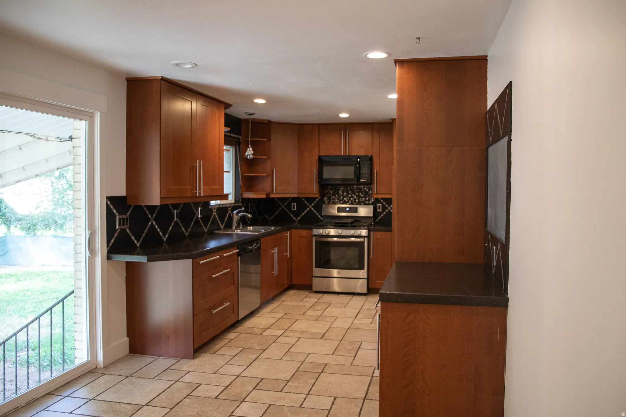 Wood-finish cabinetry with stainless steel appliances, dark countertops, and a decorative tile backsplash