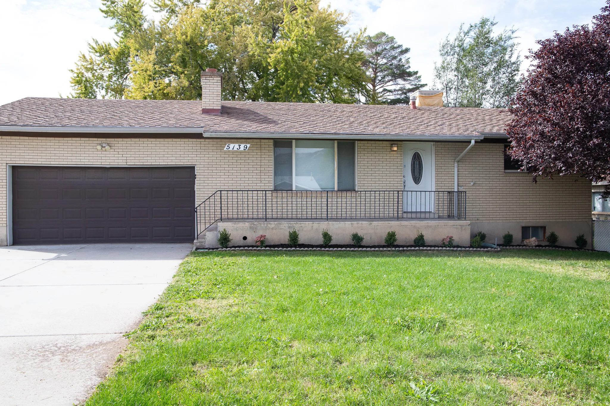 Brick exterior featuring a front porch with railing, attached garage, and concrete driveway