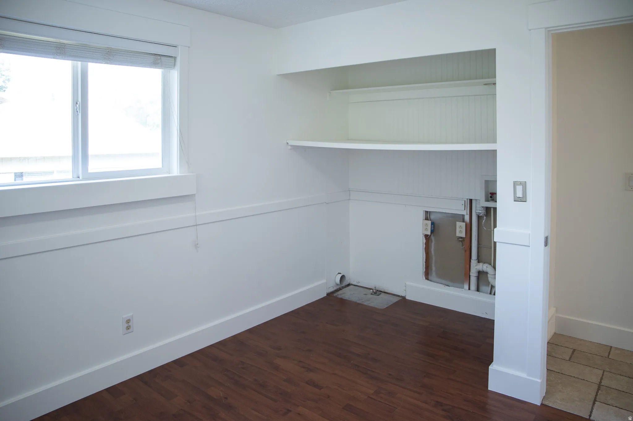 Wood-finish flooring, built-in shelving, white trim, and a window with blinds