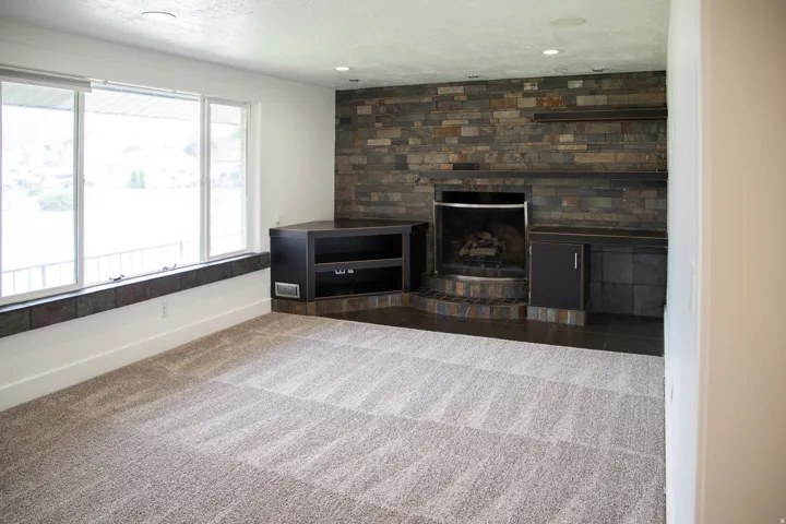 Expansive window, stone-clad fireplace, built-in cabinetry, recessed lighting, and carpet flooring