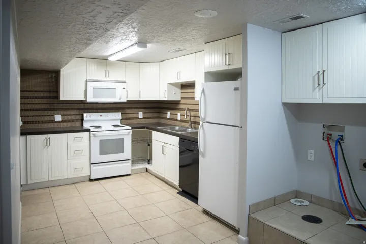 Kitchen featuring white cabinetry, dark countertops, a tile backsplash, and a white appliance package