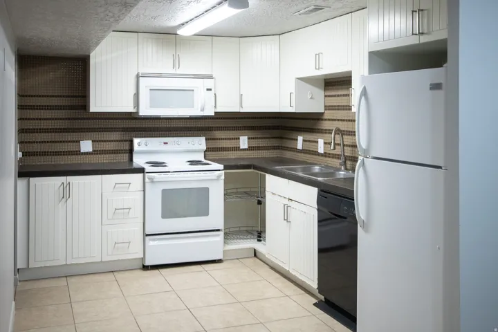 Kitchen with white cabinetry, dark countertops, tile backsplash, tile flooring, and integrated appliances