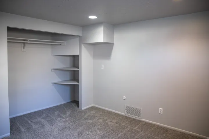 Built-in closet system with hanging rod and corner shelving, light gray wall finishes, recessed lighting, and textured carpet flooring