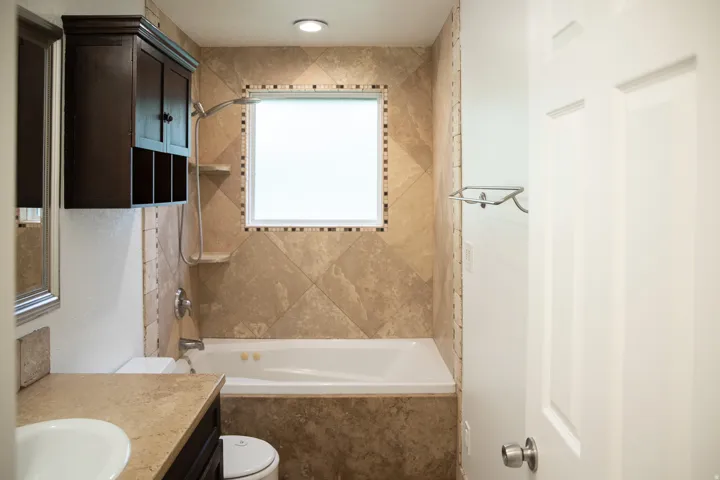 Tiled bath enclosure with a built-in tub, decorative tile accents, and an overhead shower fixture